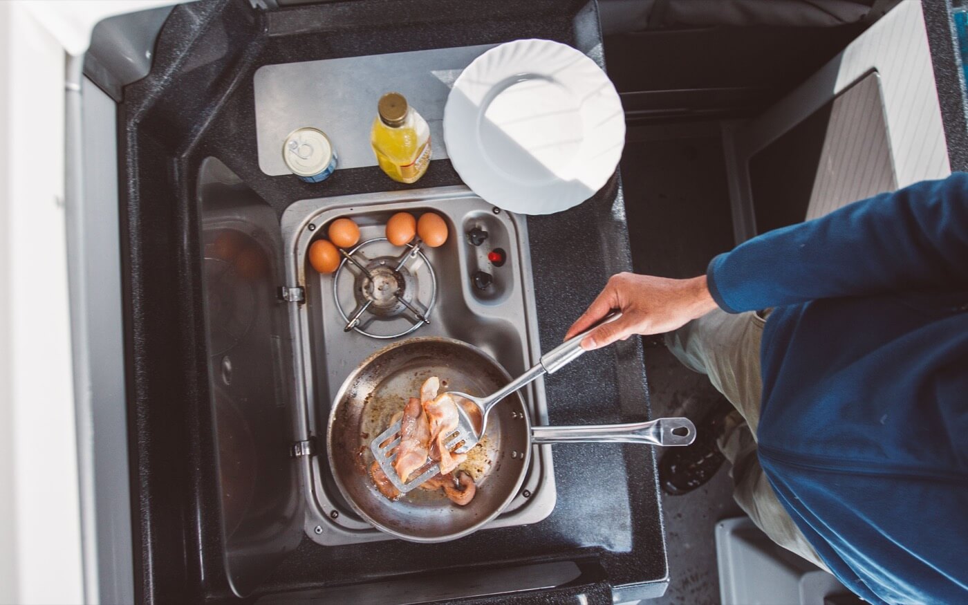 Petit-déjeuner préparé sur le réchaud compact du van avec poêle, œufs et jus