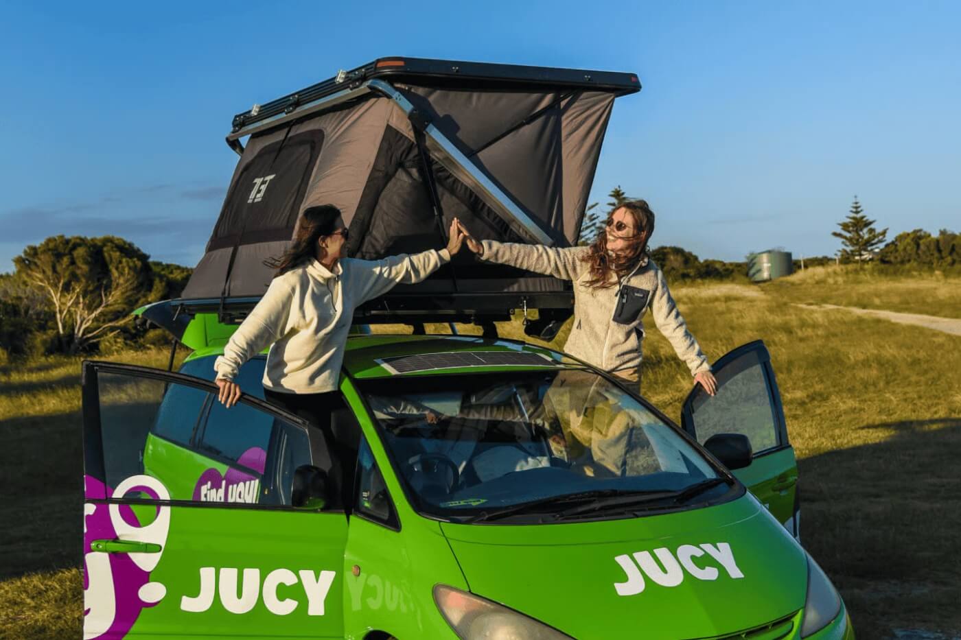 Van Jucy avec tente de toit ouverte en Australie, avec deux voyageuses près des portes du véhicule