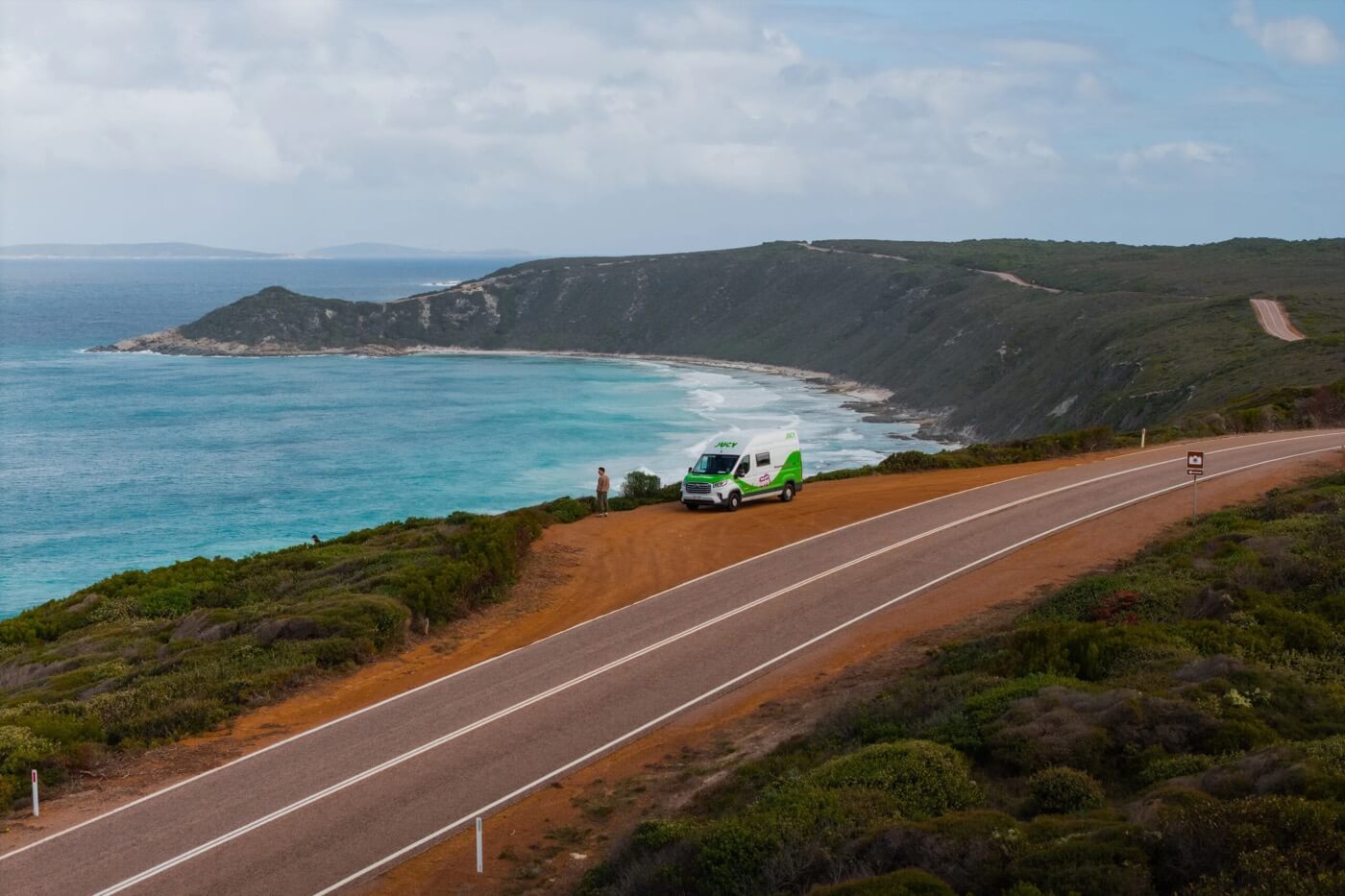 Van Jucy stationné sur un belvédère de route côtière en Australie, avec une personne face à la mer